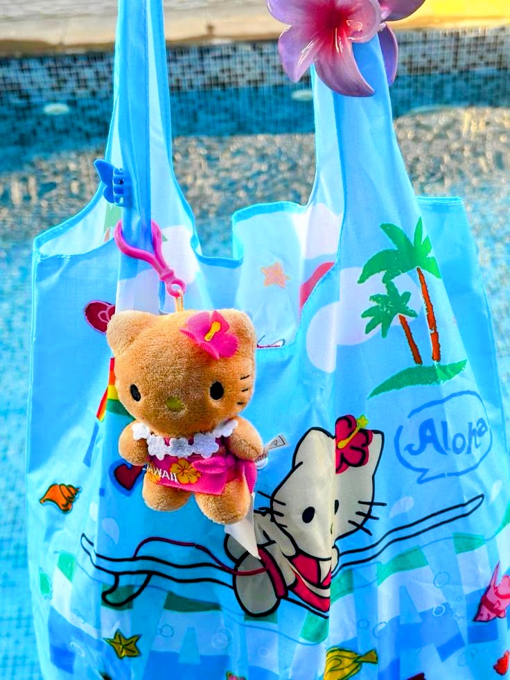 Blue Hello Kitty Aloha tote bag with tropical print and a Hello Kitty bear plush keychain attached