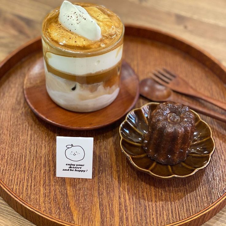 Layered iced coffee with cream and a canelé pastry on a wooden tray