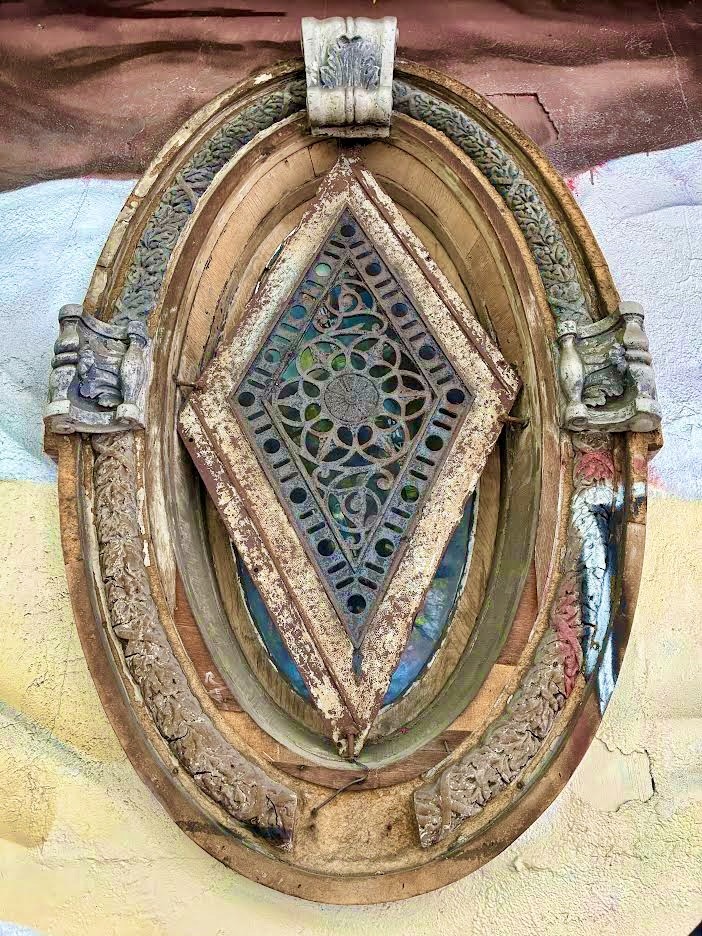 Ornate antique window with diamond stained glass in a weathered oval frame