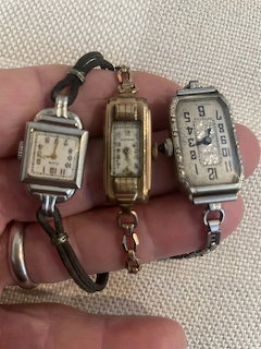 Hand holding three small vintage rectangular wristwatches with metal bands