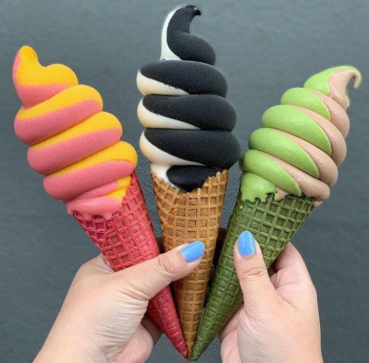 Hands holding three swirled ice cream cones in rainbow, monochrome, and pastel green colors