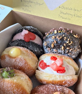 Six decorated donuts in an open bakery box with yellow sticky notes on the lid