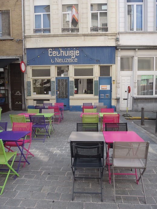 Colorful pink, green, and blue café tables and chairs on a cobblestone street in front ofEethuisje Neuzeke