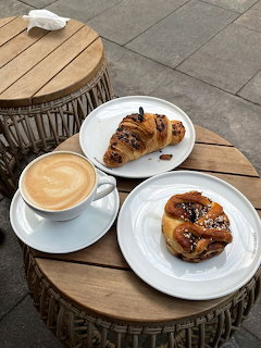 Latte and two pastries on white plates on rustic round wooden tables outdoors