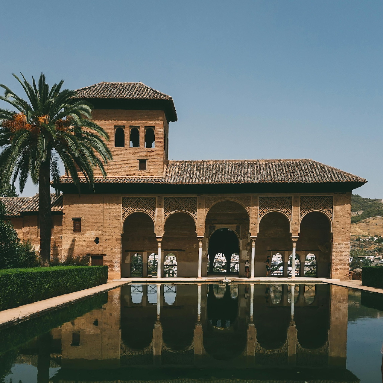 Alhambra palace facade with arches, tower, palm tree, and reflecting pool