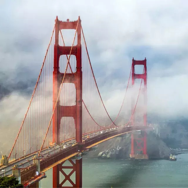 Golden Gate Bridge with red towers rising through dense fog over the water