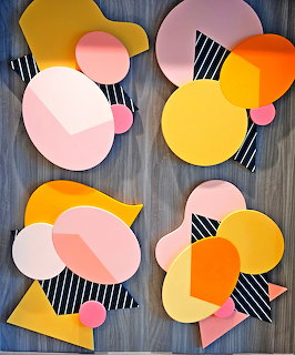 Abstract geometric art with colorful overlapping shapes including circles, triangles in pink, yellow, orange with striped patterns