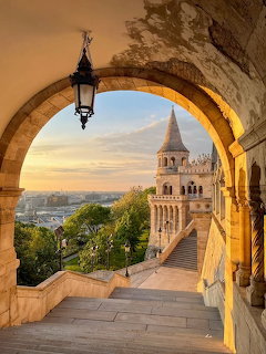 Stone archway framing Fisherman's Bastion turets in Budapest at sunset with city view
