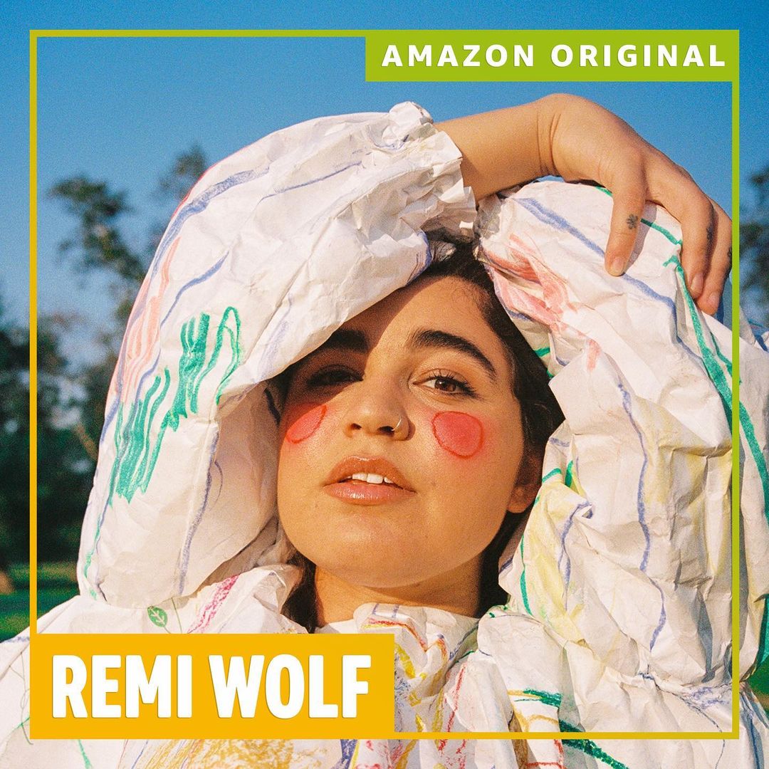 Remi Wolf posing in a white ruffled outfit with pink cheek makeup under a blue sky