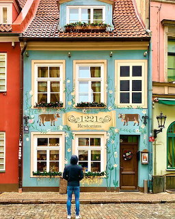 Historic blue building with decorative facade, white windows, and person viewing from cobblestone street