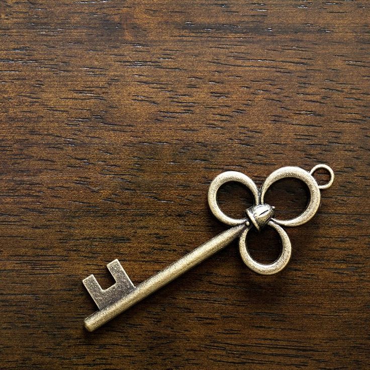 Antique brass skeleton key with three circular loops lying on dark wood grain surface
