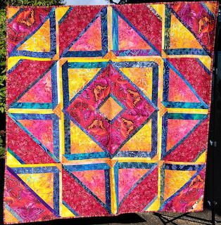 Colorful geometric quilt with diamond center and triangle border in red, pink, yellow and blue patterned fabrics