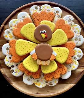 Frosted sugar cookies arranged in turkey shape with colorful feather pattern on wooden plate