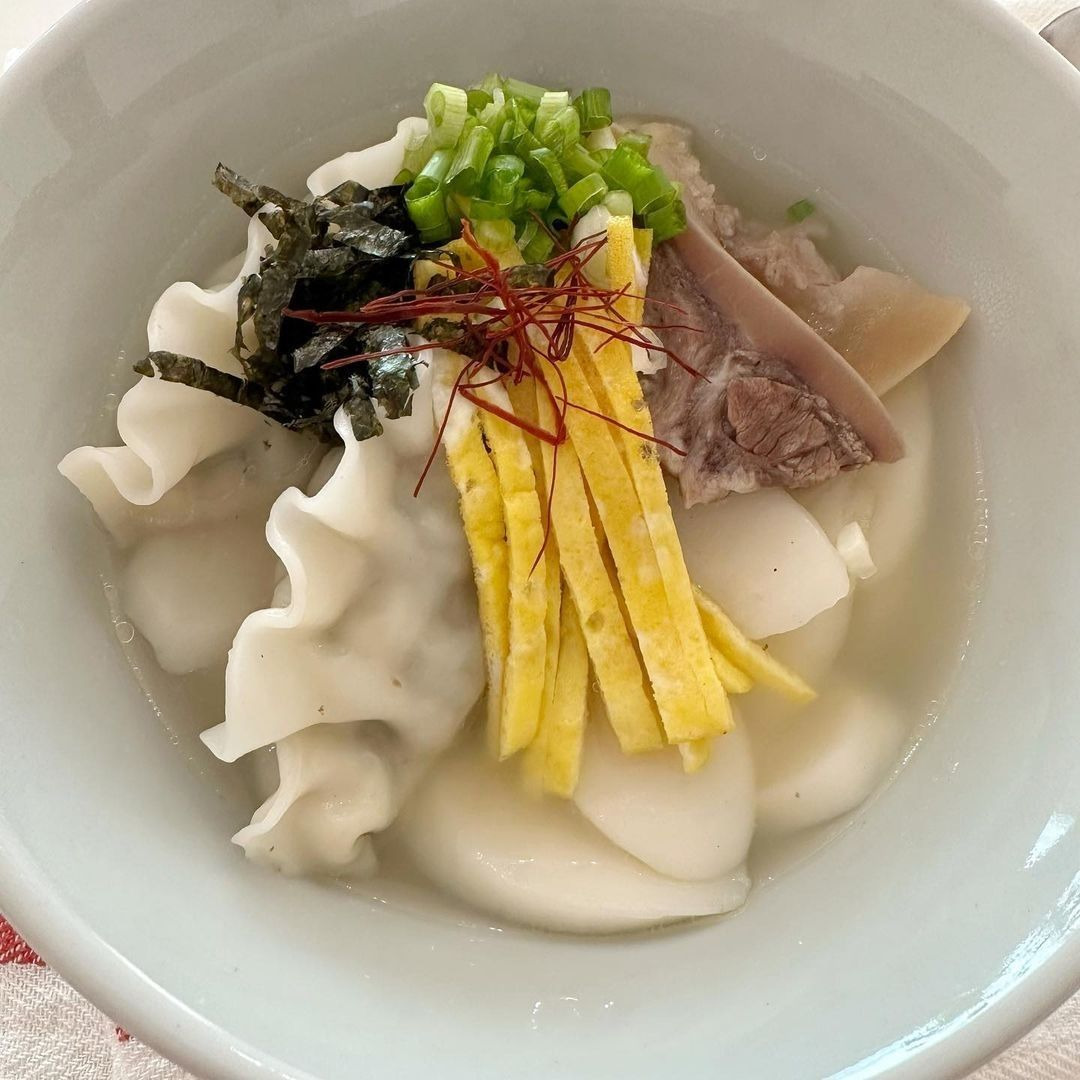 Bowl of Korean tteok mandu guk soup with rice cakes, dumplings, beef, egg, and green onions in clear broth