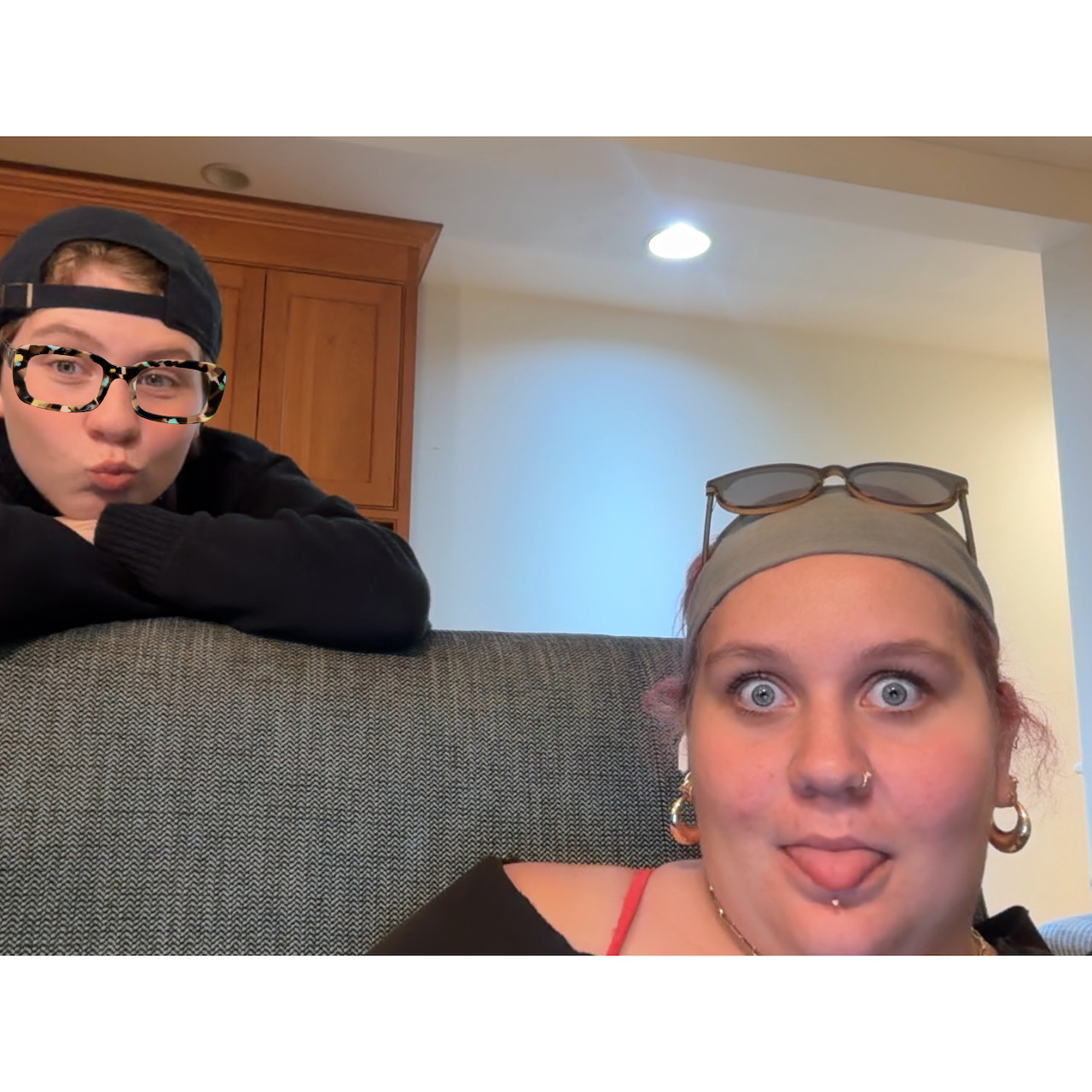 Two people indoors making funny surprised faces behind a gray couch