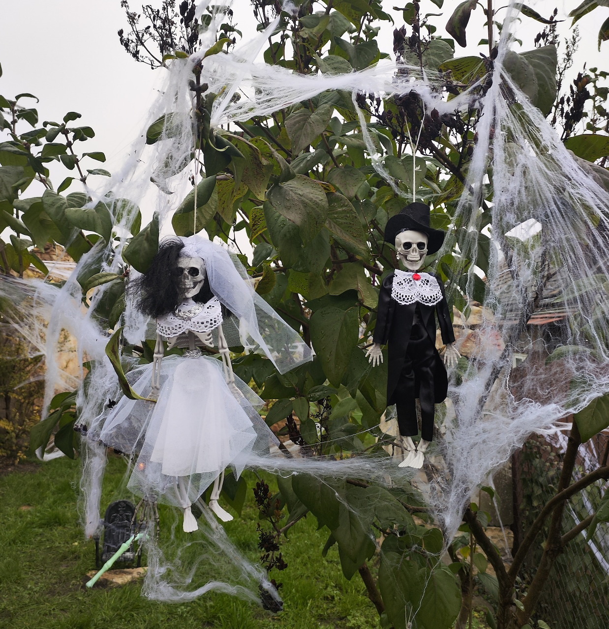 Halloween decorations with costumed figures and spider webs in garden with green plants