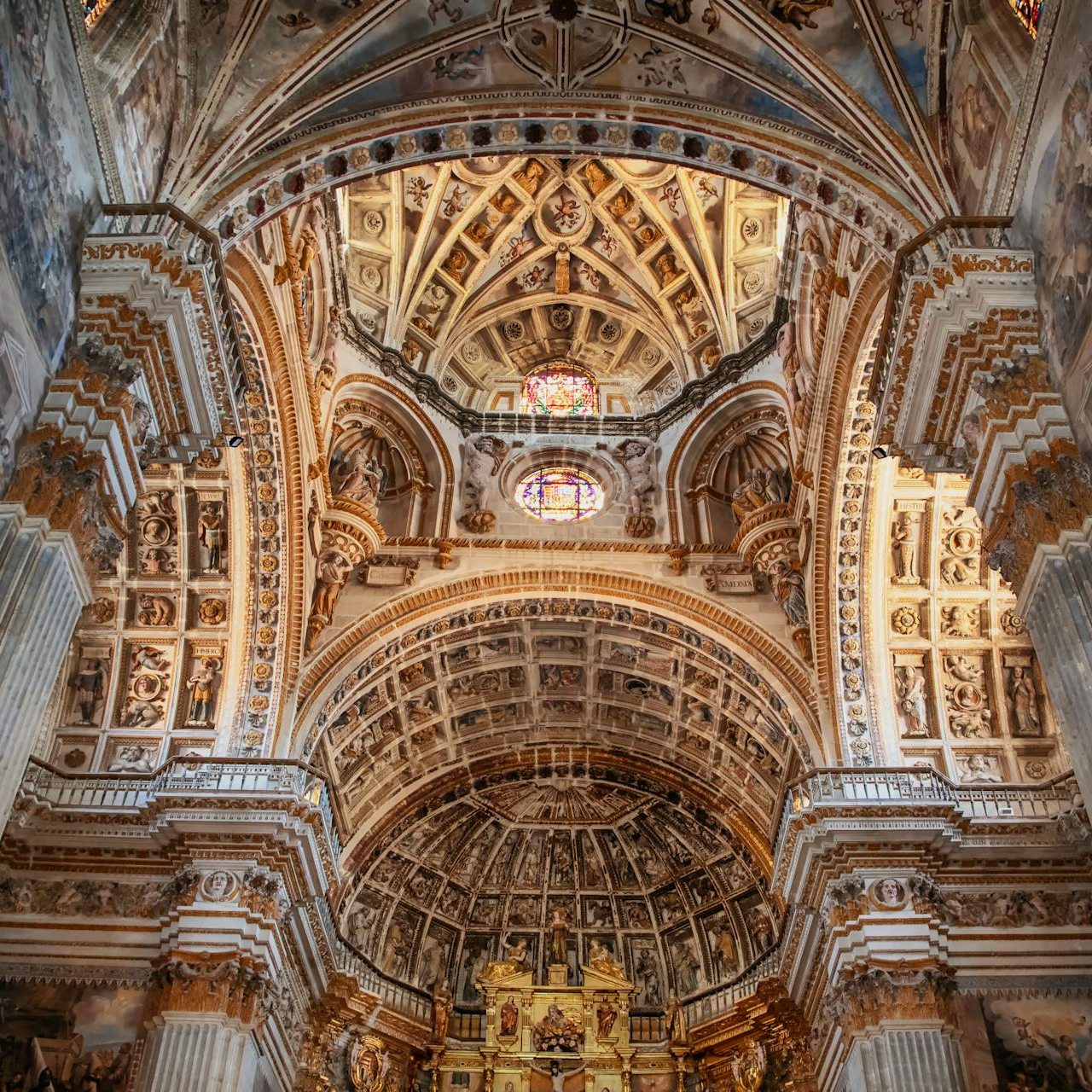 Ornate baroque church interior with golden arches and decorated dome ceiling viewed from below