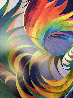 Colorful abstract quilt with swirling rainbow pinwheel patterns and curved geometric shapes in vibrant hues