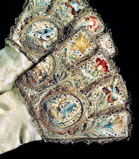 Antique embroidered gloves with ornate lace cuffs and colorful stitched designs on a black background
