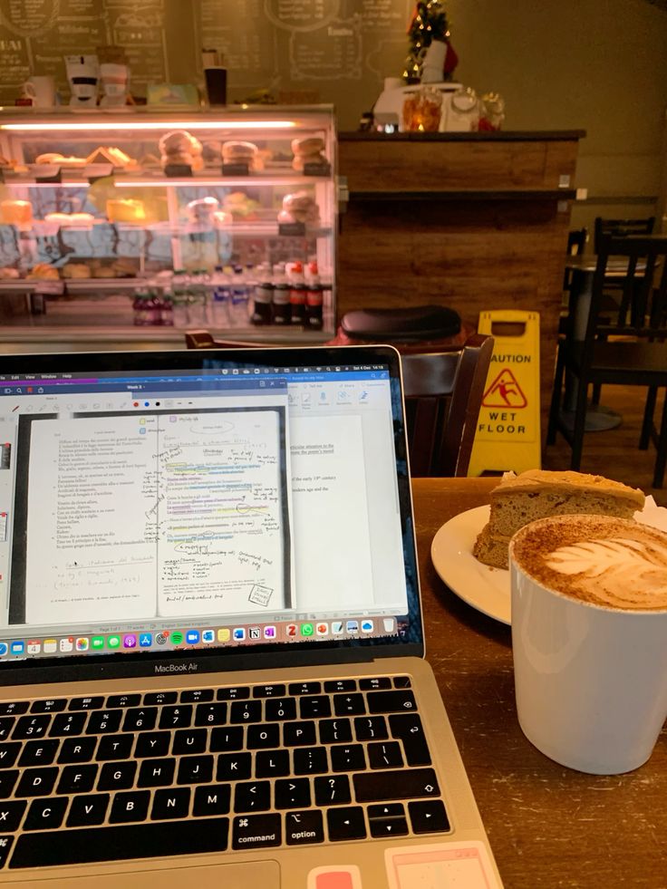 MacBook laptop and latte coffee cup on wooden table inside a cafe with display case