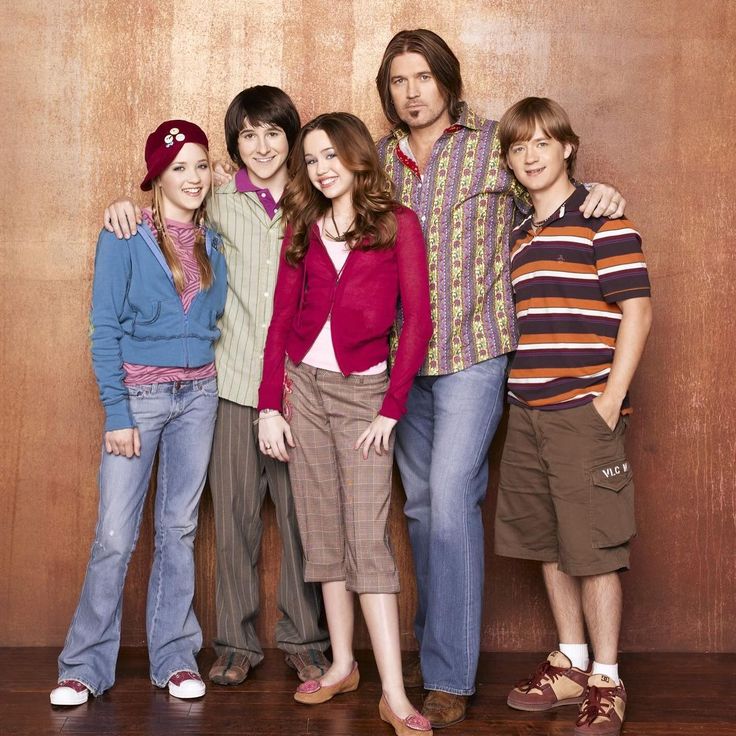 Five young actors standing together and smiling in front of a brown studio backdrop