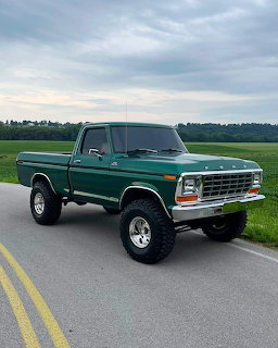 Classic green lifted Ford F-150 pickup truck parked on a rural road with fields in the background