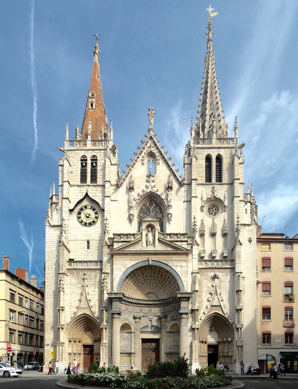 Gothic church with two tall spires, clock tower, and arched entrance in Lyon city square