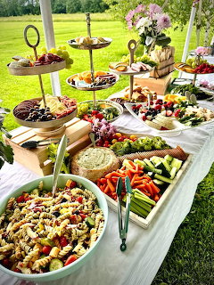 Abundant grazing table with colorful vegetables, fruits, cheeses and salads displayed outdoors on tiered serving stands