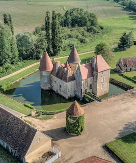 Aerial view of medieval French castle with round towers and moat surrounded by green gardens