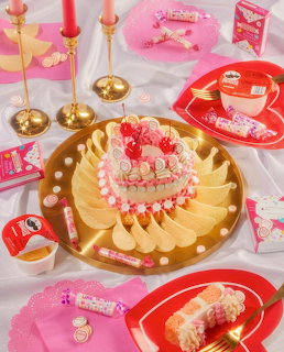 Heart-shaped pink cake on gold plate surrounded by pink candies, candles, and party decorations