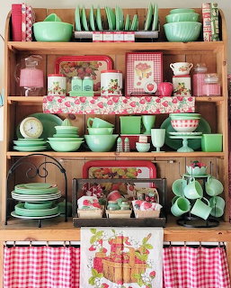 Wooden shelves with vintage jadeite dishes, strawberry-themed tins, and pink kitchen accessories