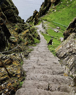 Steep stone steps climbing between tall rocky cliffs toward green hills and ocean