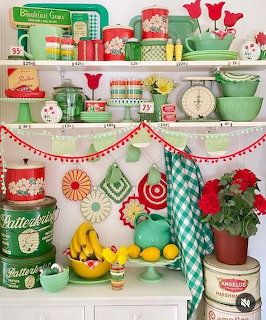 White shelves filled with colorful vintage kitchen collectibles, jadeite green dishes, retro tins, and fresh fruit