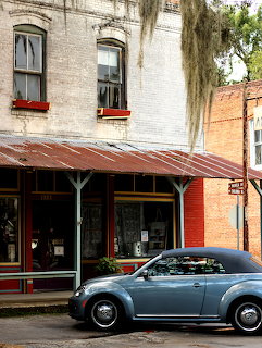 Blue vintage VW Beetle parked in front of old brick storefront with red awning