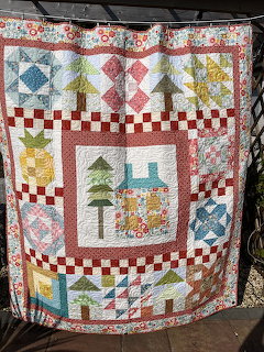 Colorful patchwork quilt with geometric blocks, appliqué house and tree, red checkered border