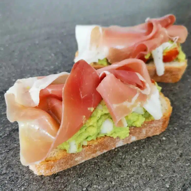 Three open-faced sandwiches topped with ham, guacamole, and cream cheese on toast