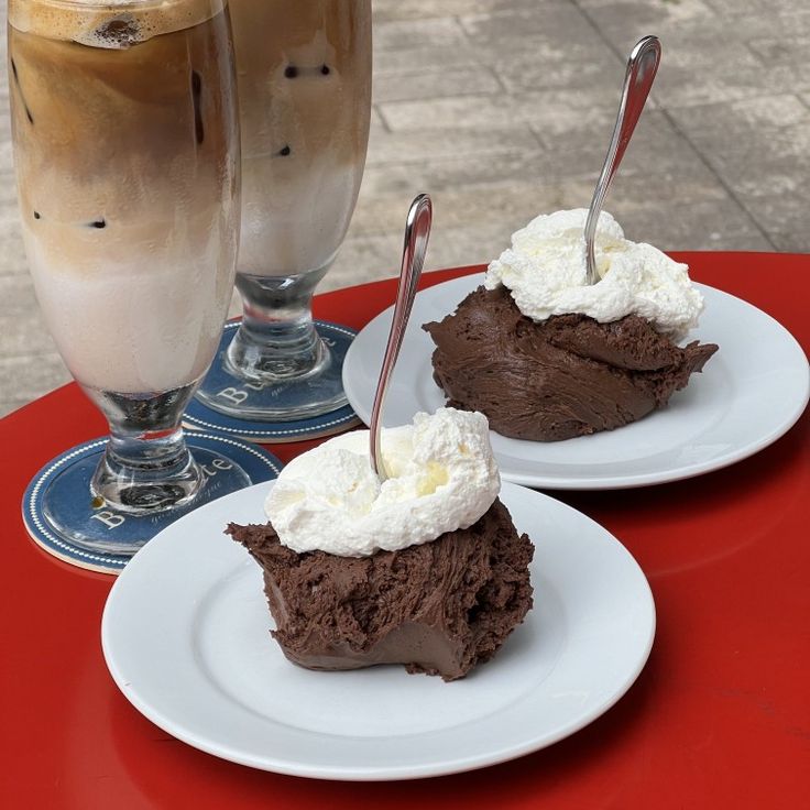 Two brownie desserts with whipped cream and two layered iced lattes on a red table