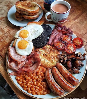 Full English breakfast plate with eggs, bacon, sausages, beans, mushrooms, tomatoes, toast and tea