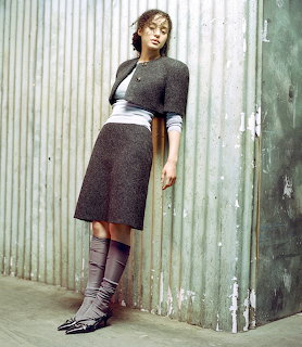 Woman in dark knit crop top and skirt standing against corrugated metal wall