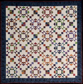 Colorful patchwork quilt with repeating geometric crown crossing pattern and dark blue border