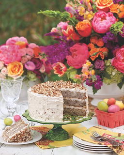 Layer cake on a stand beside a bright flower bouquet, plates, and pastel eggs on a table