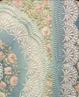 Close-up of a long arm quilt with rose fabric, lace fan motifs, and feather quilting in pastel blue and pink tones