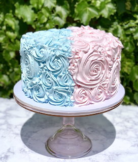 Gender reveal cake with blue and pink rosette frosting on glass cake stand