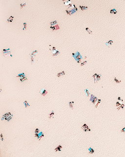 Aerial overhead view of beachgoers scattered on light sand with colorful towels