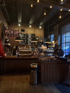 Interior of a cozy coffee shop with wooden counter, espresso machines, pastry case, and string lights