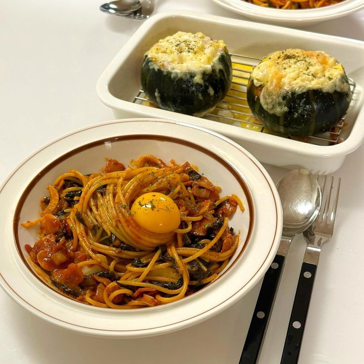 Bowl of spicy noodles with egg yolk beside two stuffed vegetable cups on a white table
