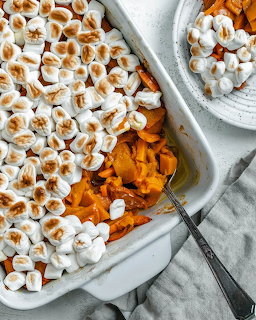 Overhead view of candied yams topped with toasted marshmallows in a white baking dish with a serving on a plate
