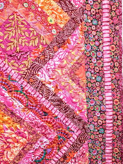 Diagonal strips of pink and orange patchwork fabric with floral patterns and decorative beading