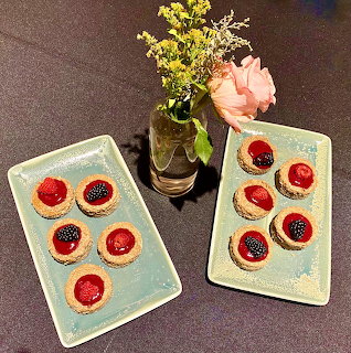 Two rectangular plates with fruit-topped biscuits beside a glass vase with pink and yellow flowers