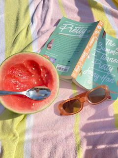 Halved watermelon with spoon, sunglasses, and book on a colorful striped beach towel